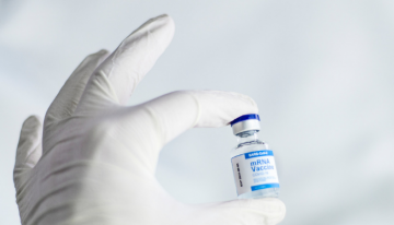 White gloved hand holding up an mRNA vaccine vial