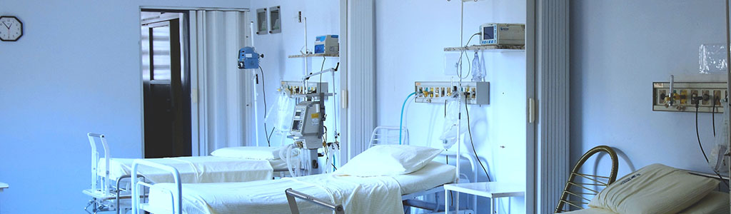 Empty hospital beds in a white room, with medical equipment. Used to illustrate how design influences healthcare in hospitals.
